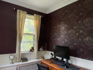 Corner view of the desk, window and wallpapered wall.